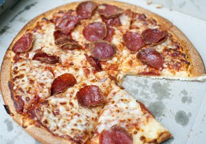 Close up view of a takeaway cheese and pepperoni or salami pizza sliced into portion with one slice removed still in the traditional disposable cardboard pizza box