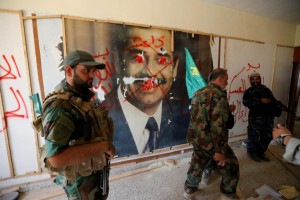 Fighters from the Iraqi Shi'ite Badr Organization walk past a poster depicting images of former Iraqi President Saddam Hussein on the outskirts of Falluja