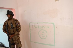 A member of the Iraqi security forces stands next to a drawing on a wall of a flag used by Islamic State militants, south of Falluja