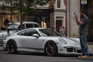 A man takes a photo of a Porsche GT3 on Sloane Street in London, England on August 09 2016.